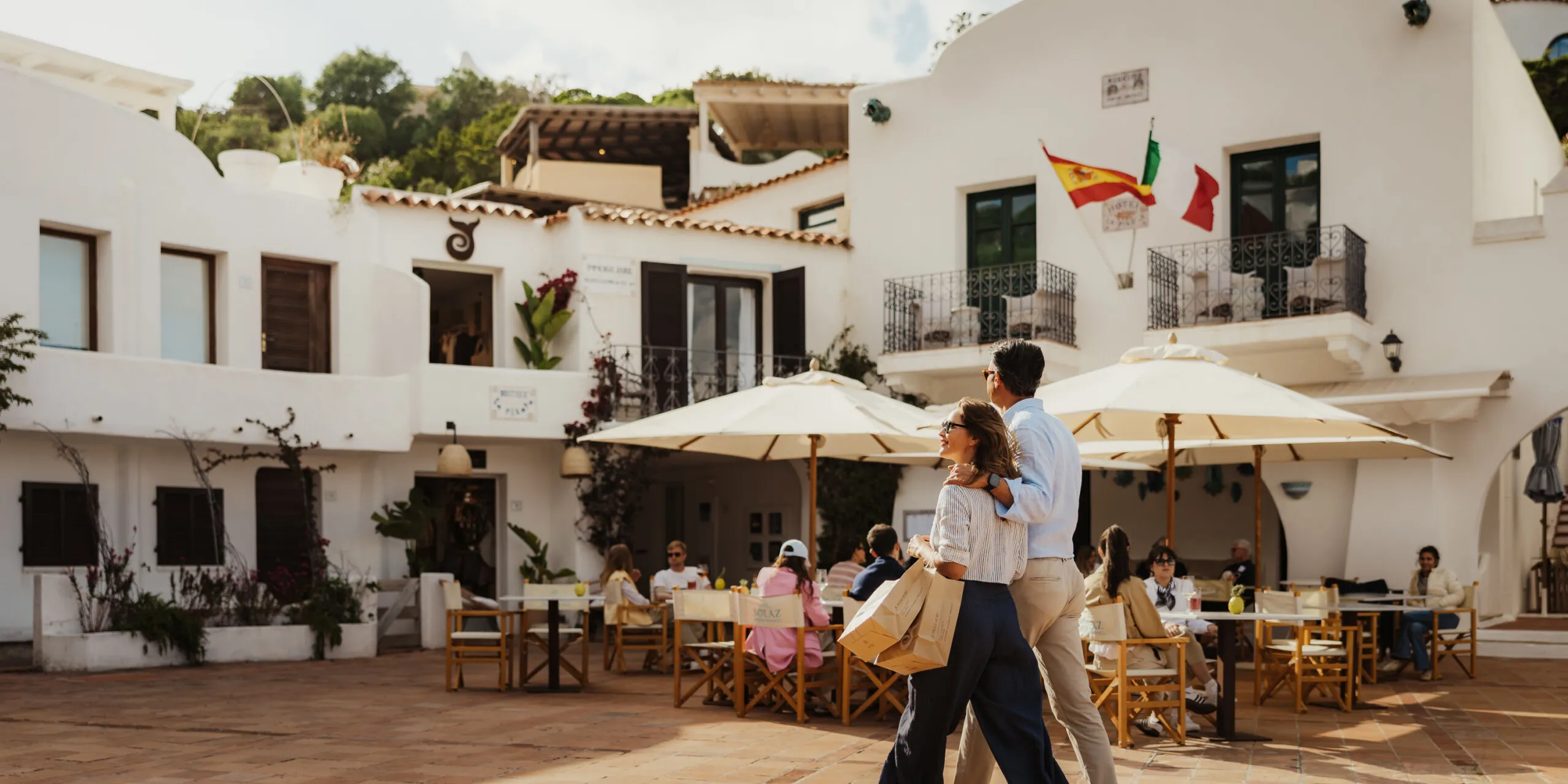 A couple strolls through the courtyard of a white building in Porto Rafael's piazzetta, surrounded by charming architecture.