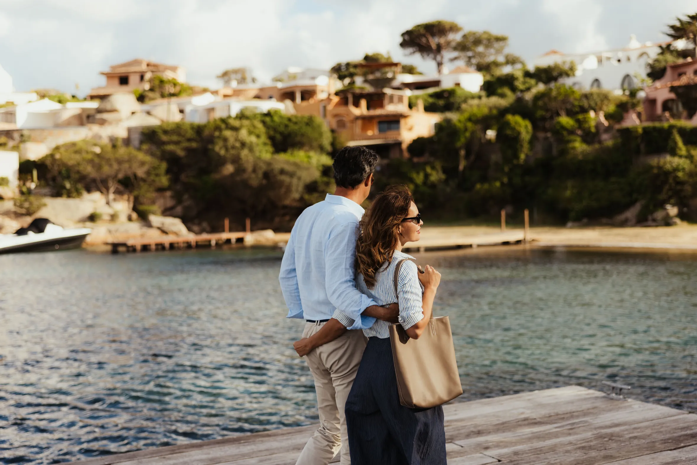 In Porto Rafael a couple stands on the dock, gazing at the water, surrounded by a serene coastal landscape.