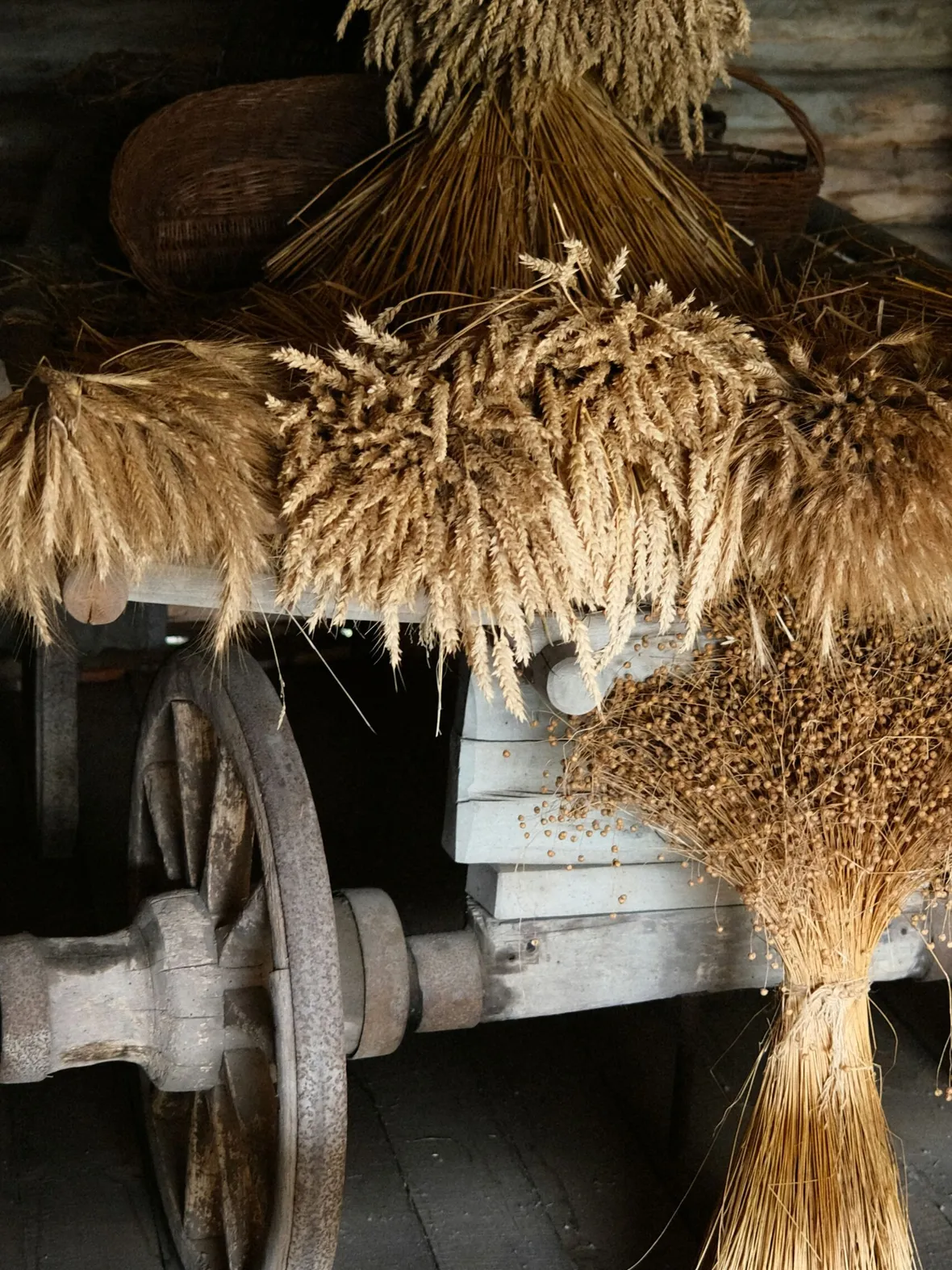 A rustic cart with bundles of wheat and grain sheaves arranged on top and sides. The wooden wheels and earthy tones evoke a vintage, agrarian feel.