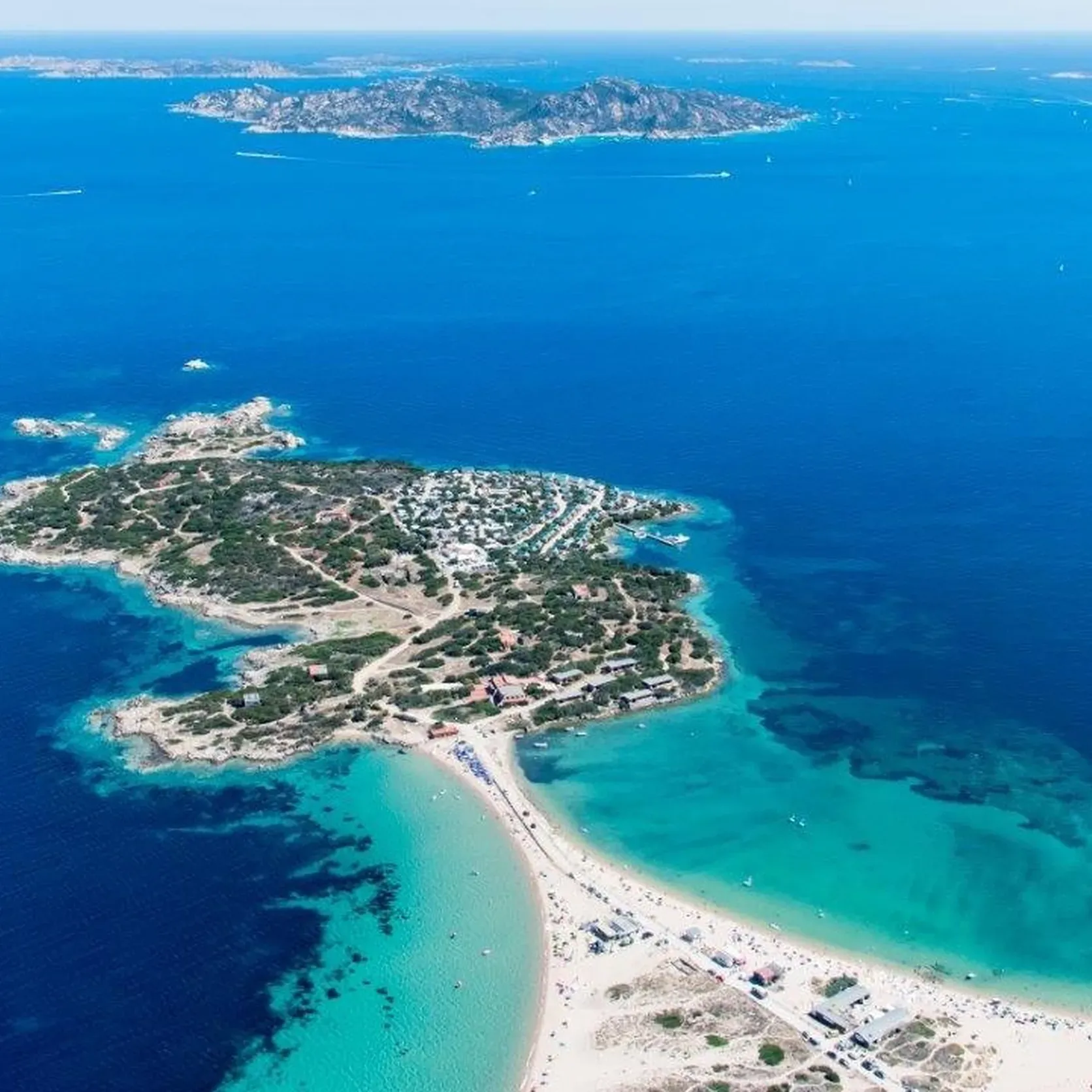 Aerial view of a picturesque island surrounded by turquoise and deep blue ocean waters. Sandy beaches curve around lush greenery, conveying a serene, tropical vibe.