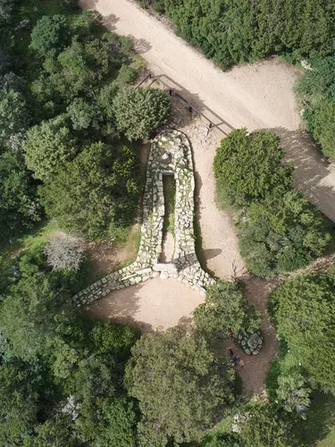 Aerial view of a stone structure shaped like a keyhole surrounded by lush green trees. A dirt path runs alongside, creating a serene, natural setting.