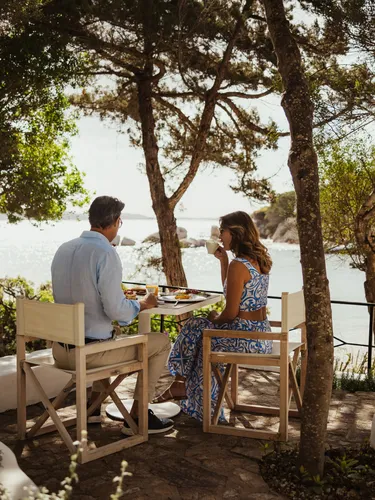 A couple enjoys breakfast at a table with an ocean view at Hotel La Piazza in Porto Rafael.